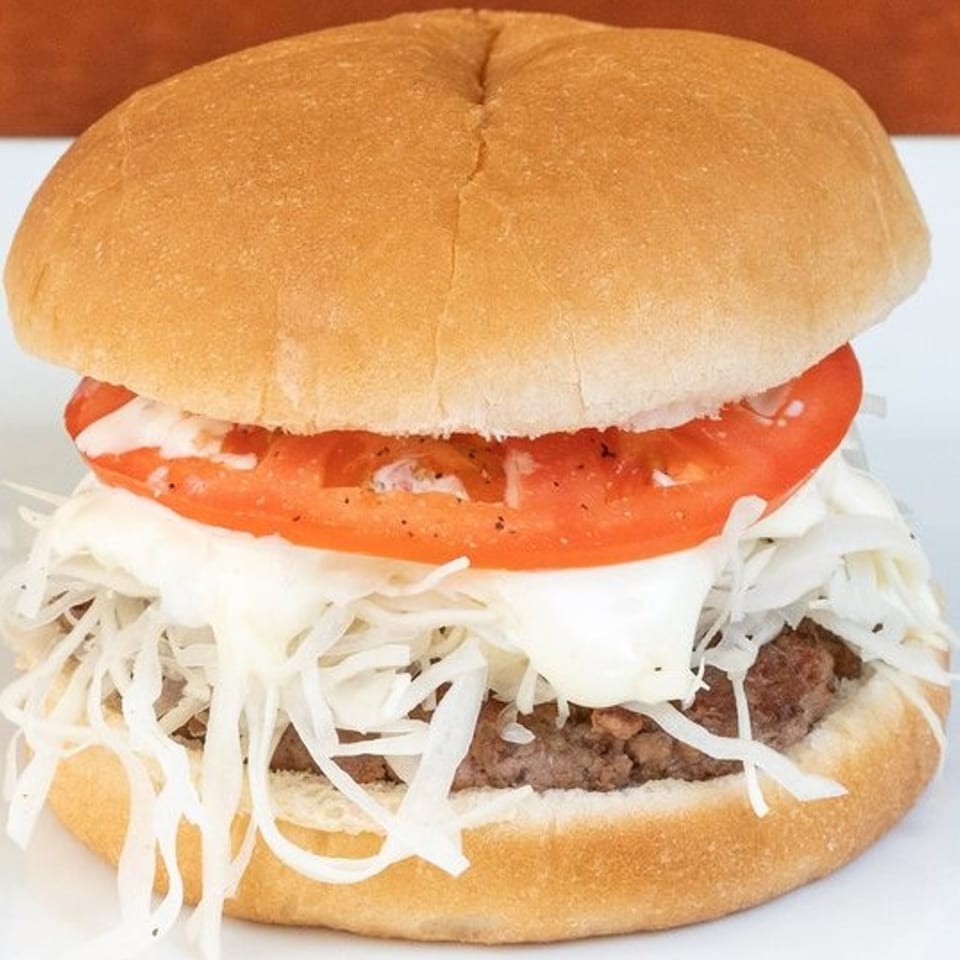 A Texas Ranger burger with a patty, shredded cabbage, tomato, and white sauce on a bun.