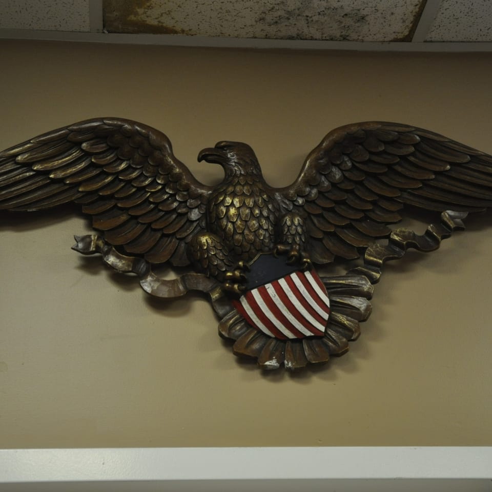 A bronze American eagle with outstretched wings holds a red, white, and blue shield.