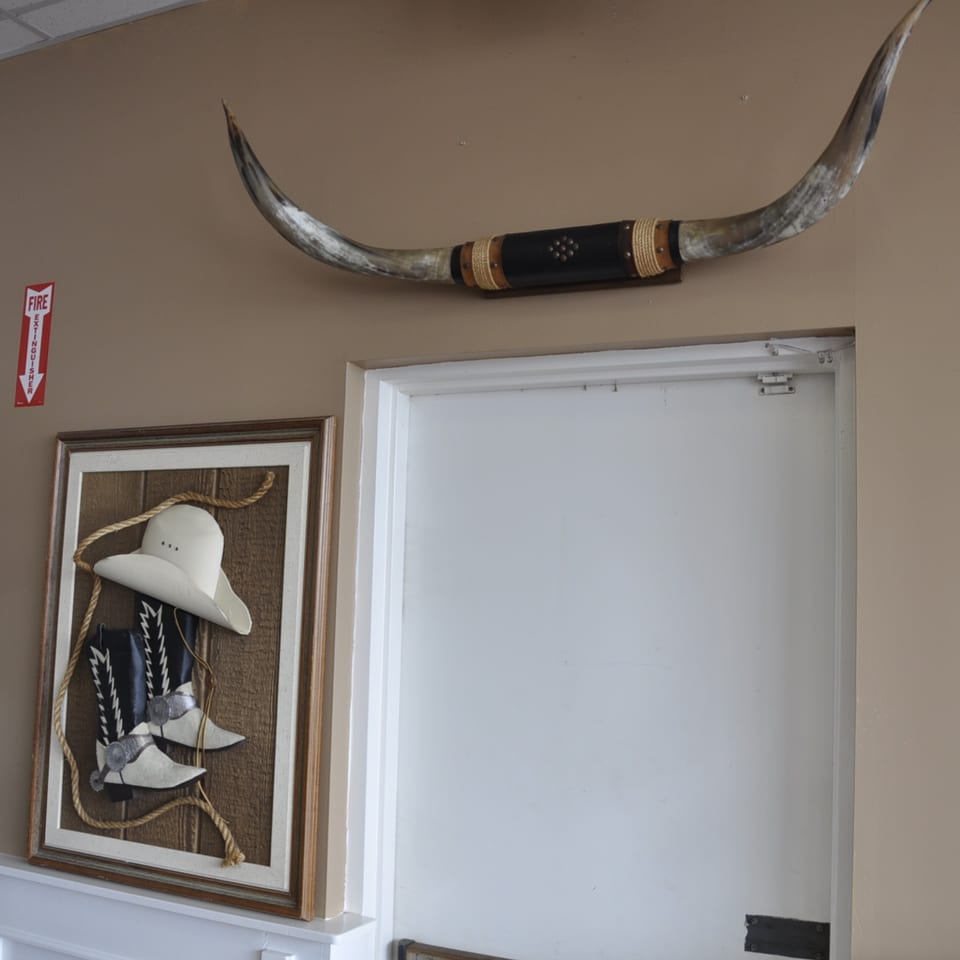 Longhorn horns mounted above a framed display of a cowboy hat, boots, and rope.