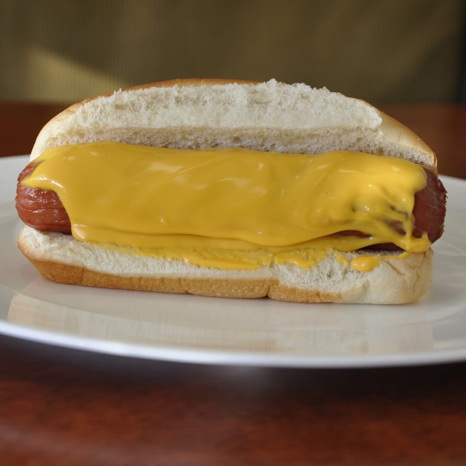 A Texas Ranger hot dog with melted cheese in a bun on a white plate.