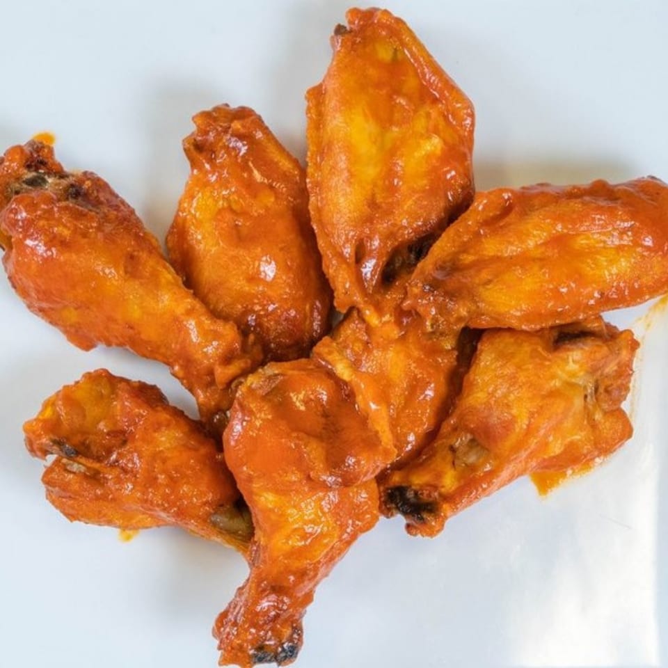 Six buffalo chicken wings, coated in a vibrant orange sauce, arranged on a white surface.