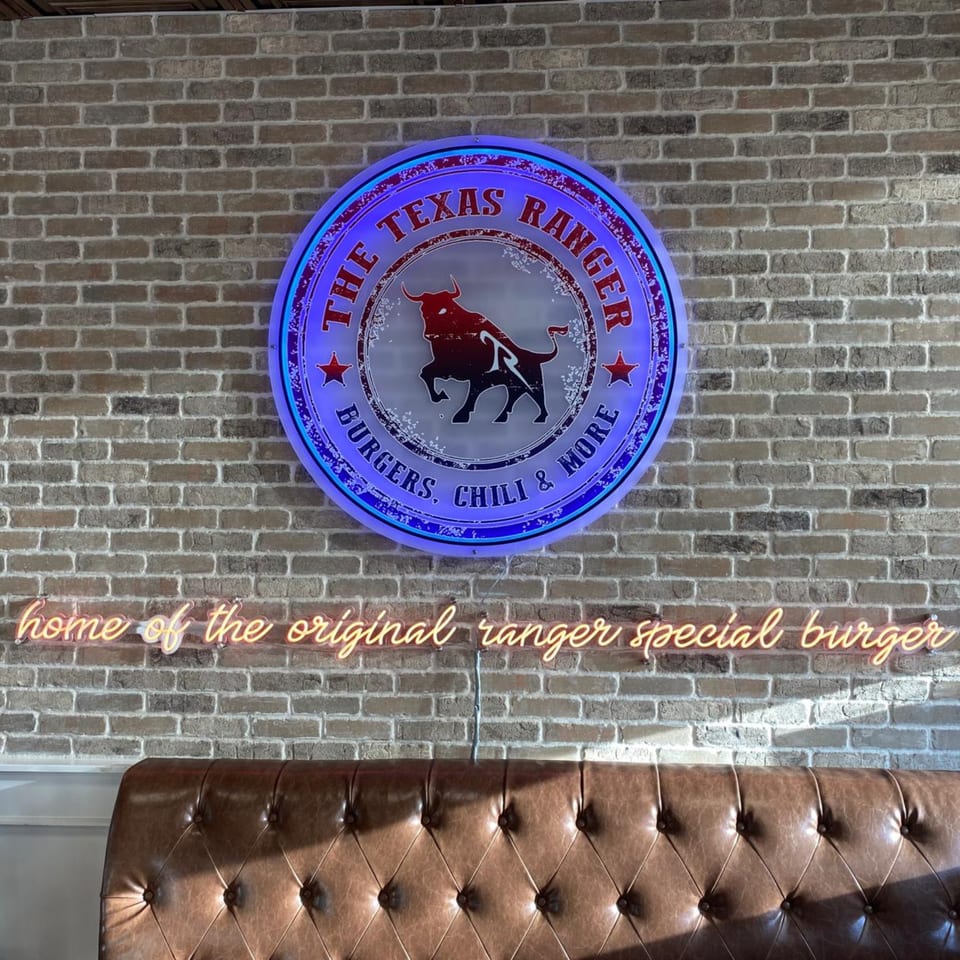 The Texas Ranger neon sign with a bull logo and a neon sign for "original ranger special burger" above a brown booth.