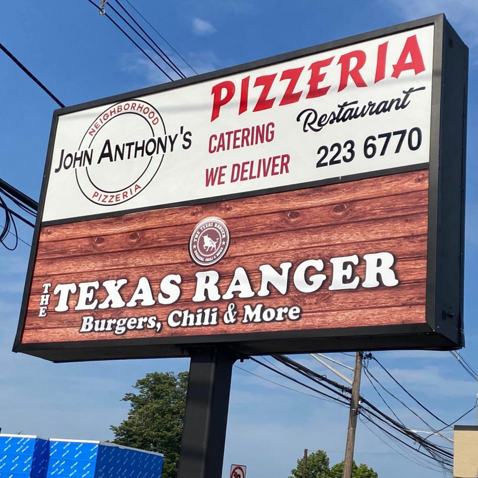 A large outdoor sign for John Anthony's Pizzeria and The Texas Ranger, advertising burgers, chili, and more.