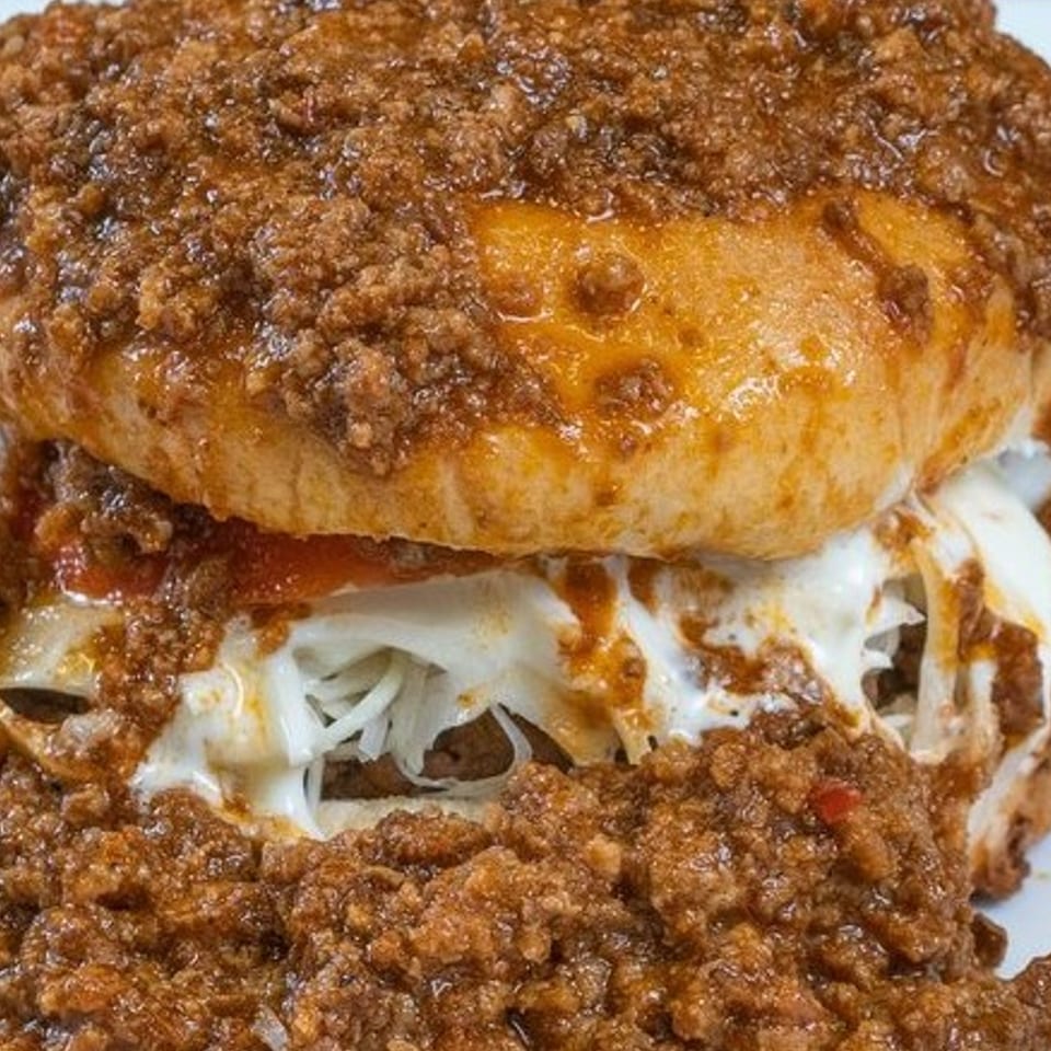 Close-up of a Texas Ranger chili burger, overflowing with melted cheese and savory chili.