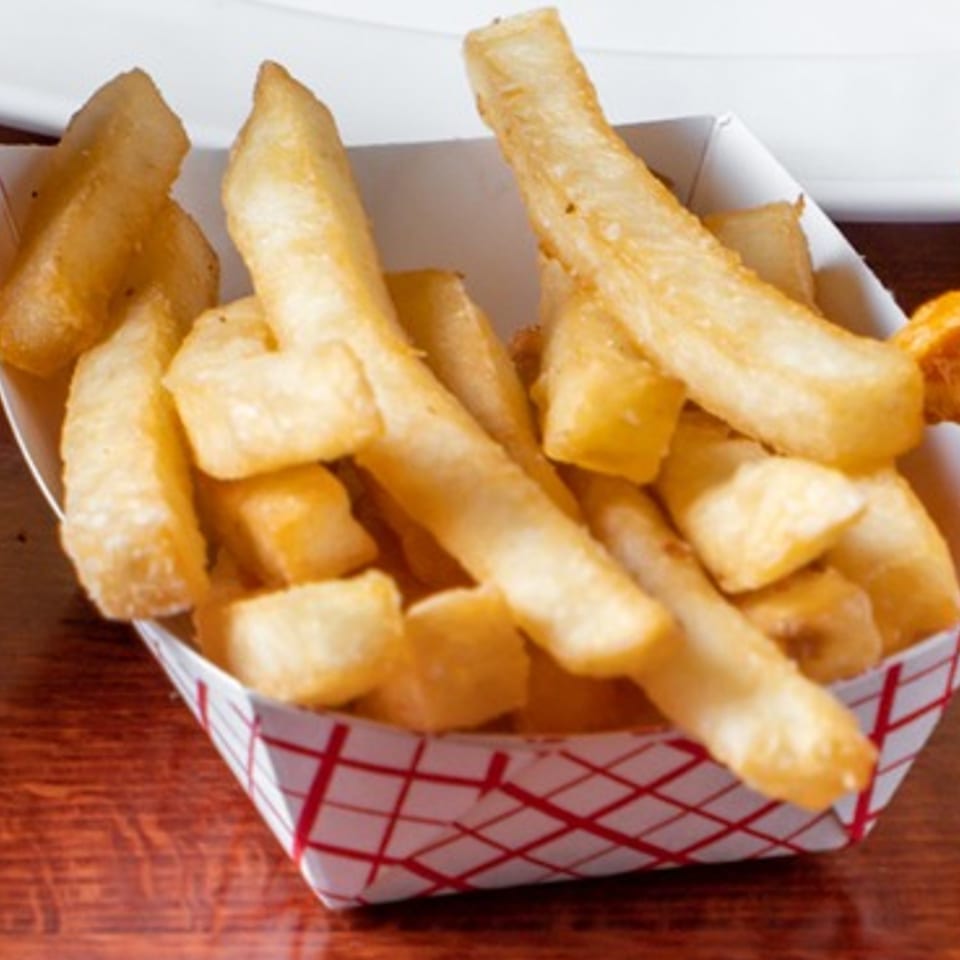 Golden-brown, thick-cut French fries in a white paper tray with red checkered pattern.