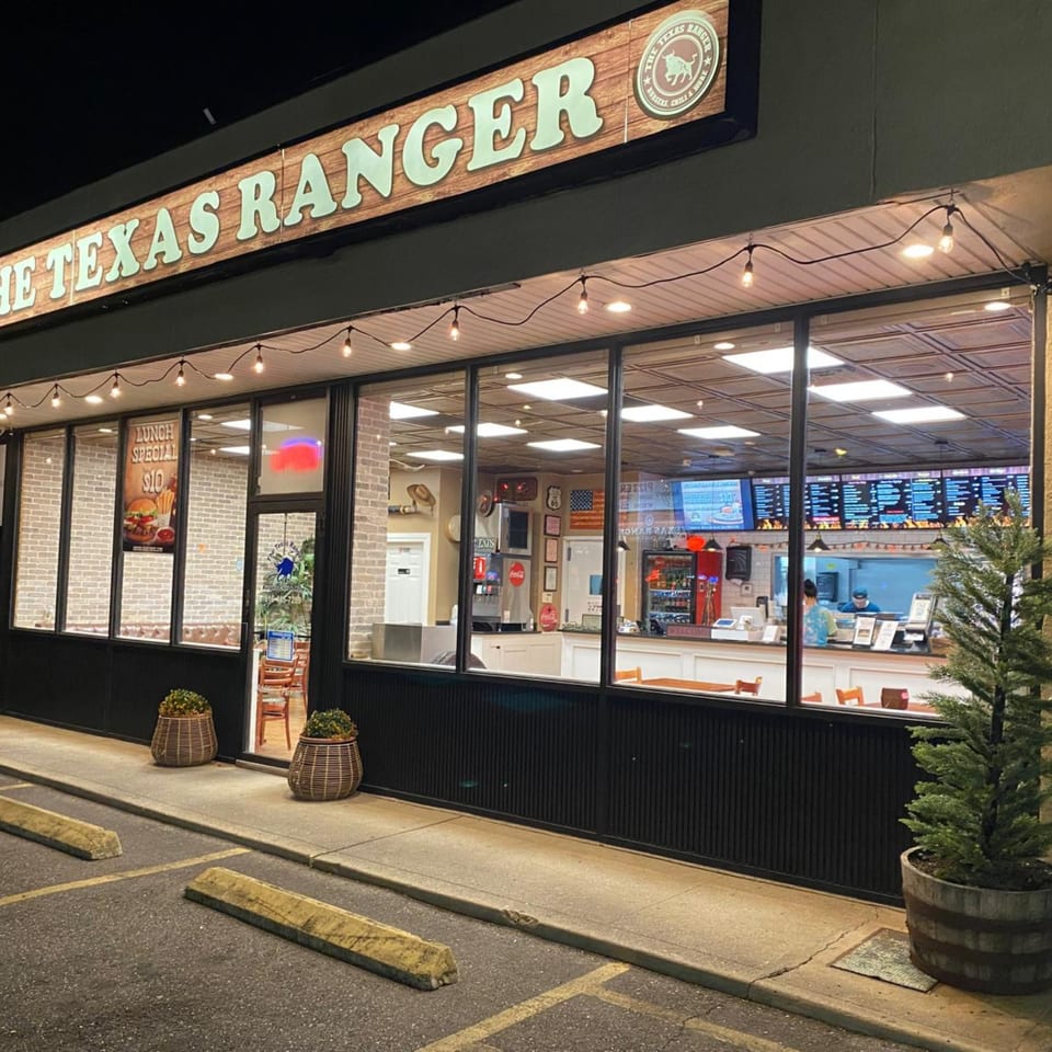 Exterior of The Texas Ranger burger restaurant at night, with a lit-up sign and visible interior.