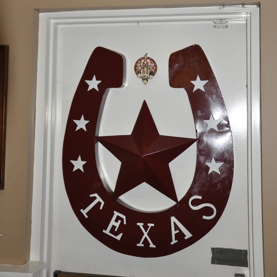 A white door with a large brown horseshoe and star logo, spelling "TEXAS" at the bottom.