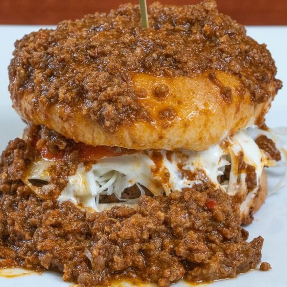 A Texas Ranger chili burger, overflowing with chili and melted cheese, on a white plate.