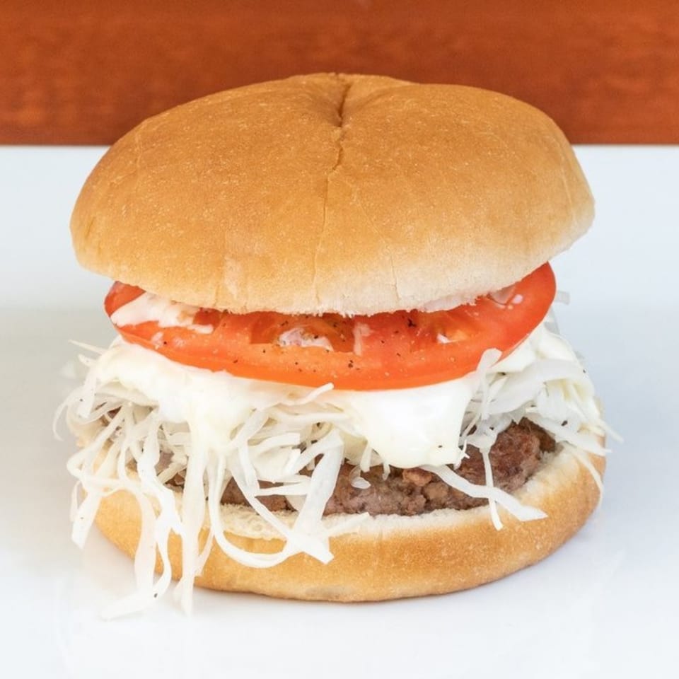 A Texas Ranger burger with a beef patty, shredded cabbage, mayonnaise, and a tomato slice.