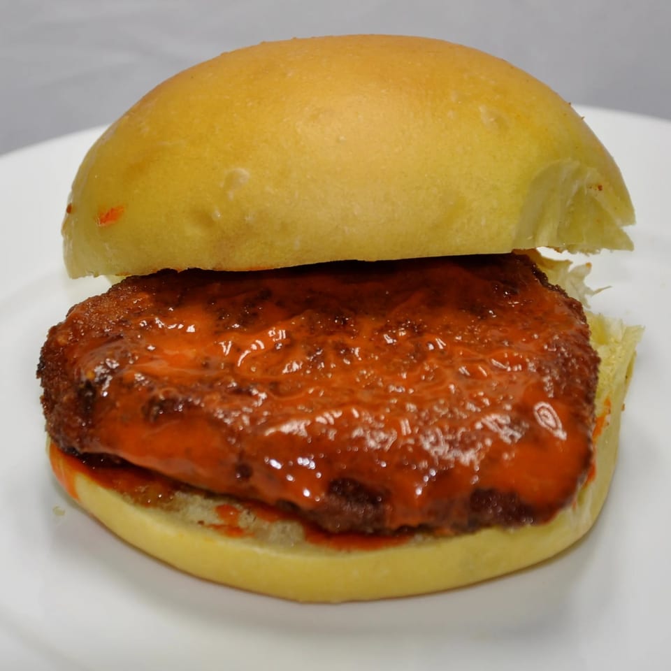 A Texas Ranger burger with a crispy patty covered in a vibrant orange sauce on a white plate.