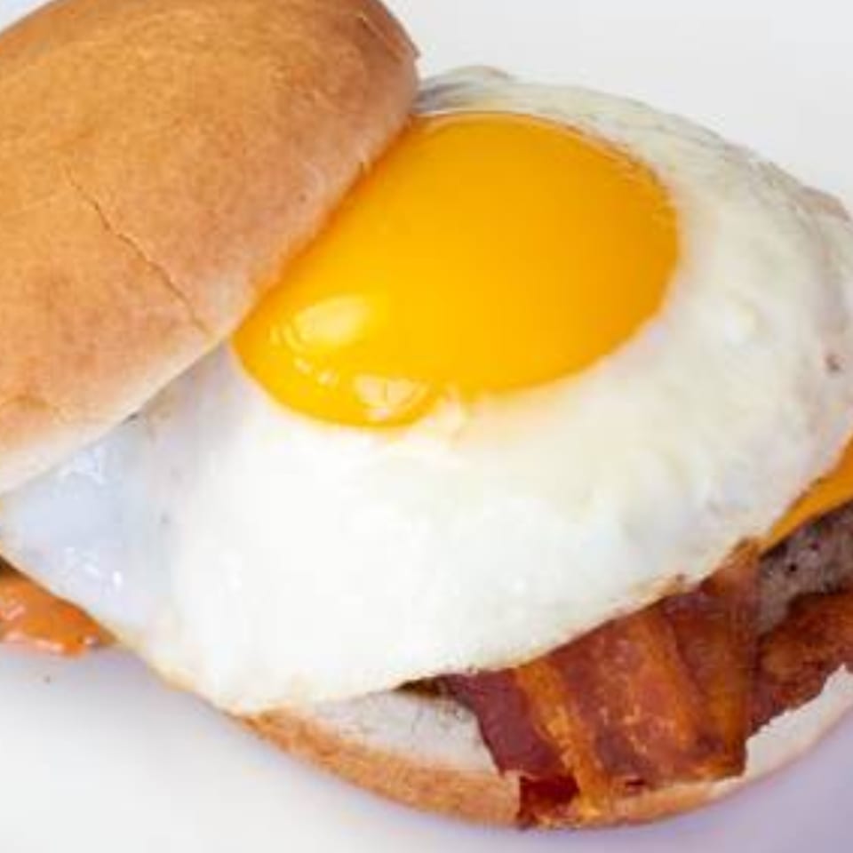 A close-up of a breakfast burger with a fried egg, bacon, and cheese on a bun.