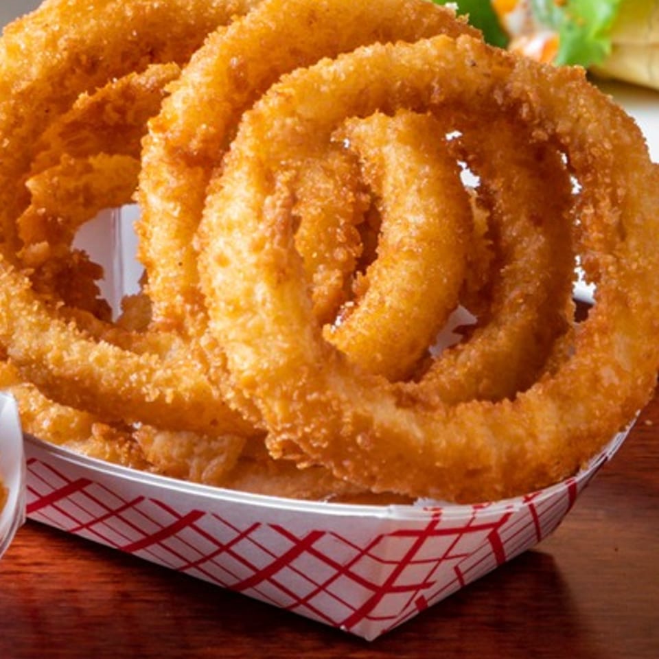 Golden-brown, crispy onion rings from The Texas Ranger, served in a red and white checkered paper tray.