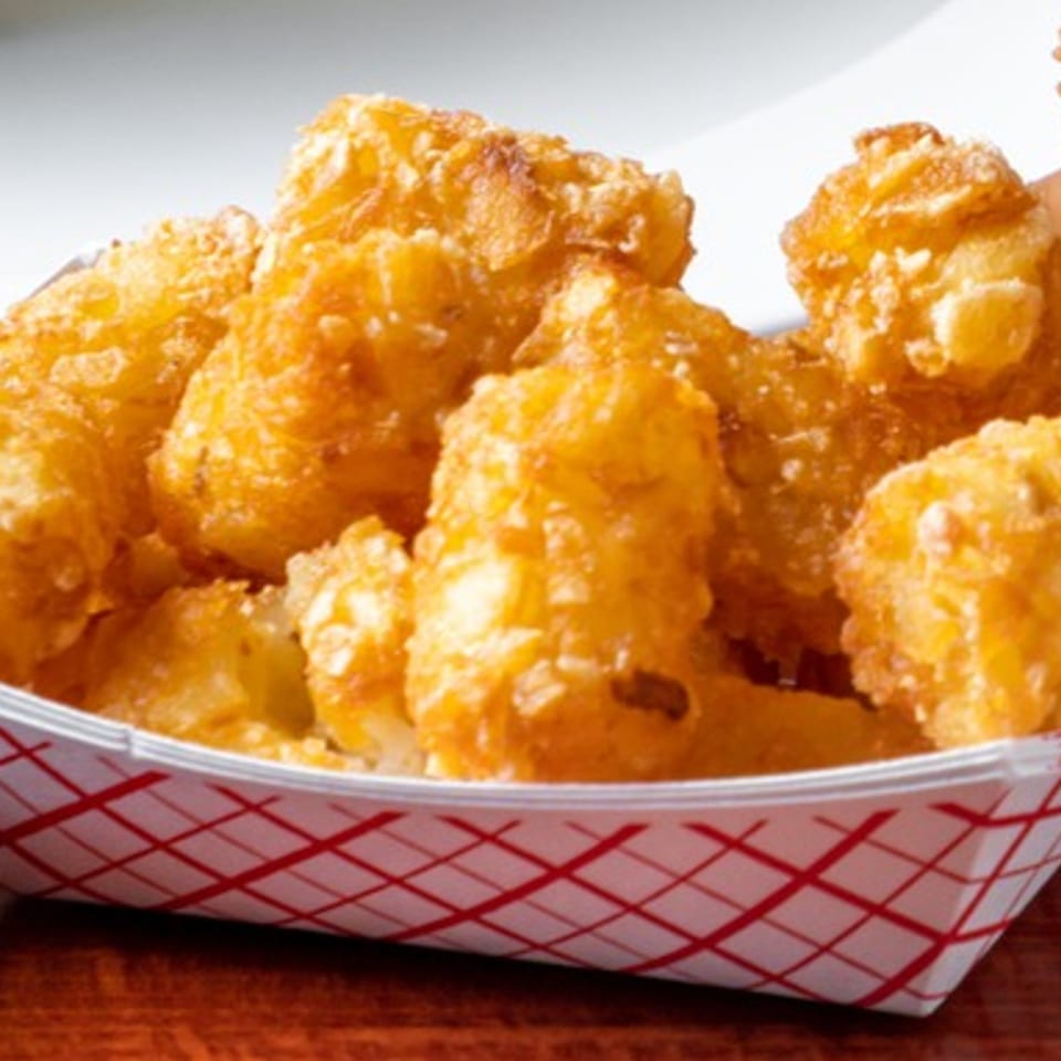 Golden-brown tater tots in a red and white checkered paper tray from The Texas Ranger.