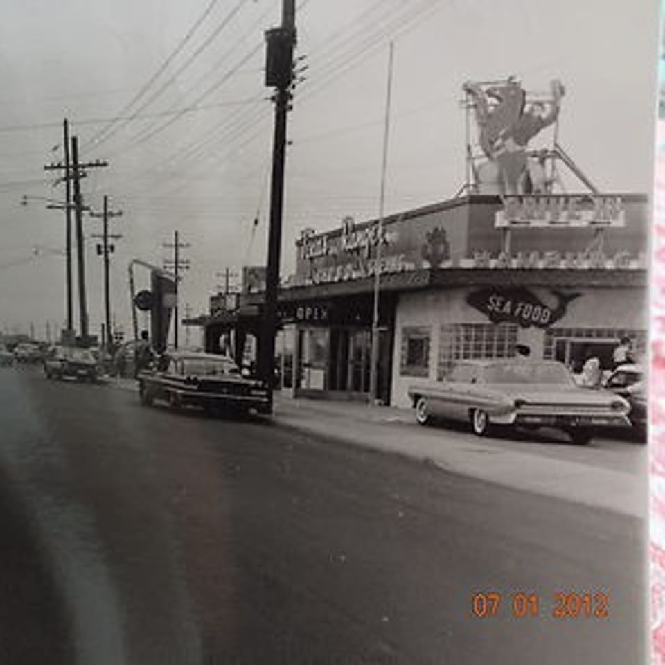 Vintage black and white street view of The Texas Ranger burger restaurant with classic cars parked.