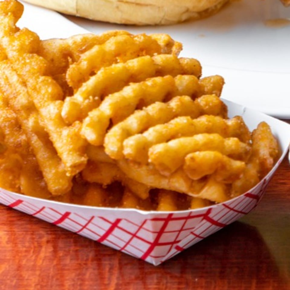 Crispy golden waffle fries in a red and white checkered paper tray on a wooden table.