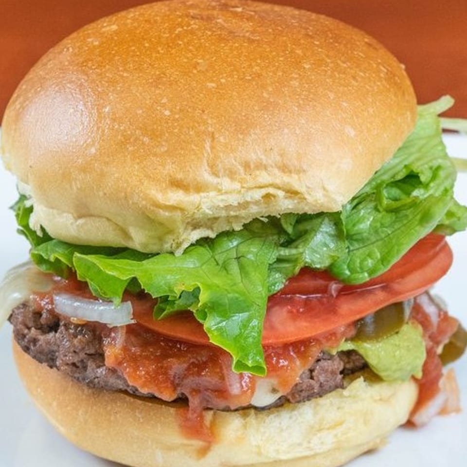 A Texas Ranger burger with lettuce, tomato, onions, guacamole, and jalapeños on a bun.