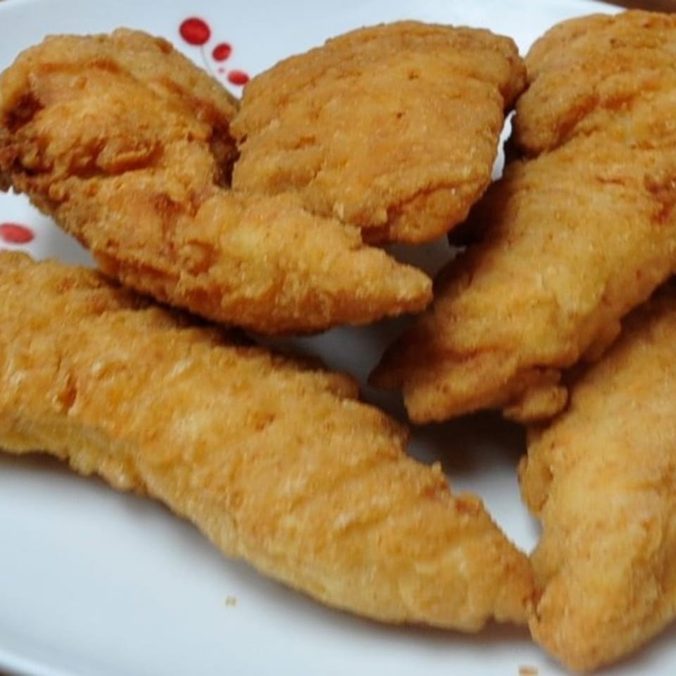 Golden-brown fried chicken tenders or fish fillets on a white plate with red polka dots.