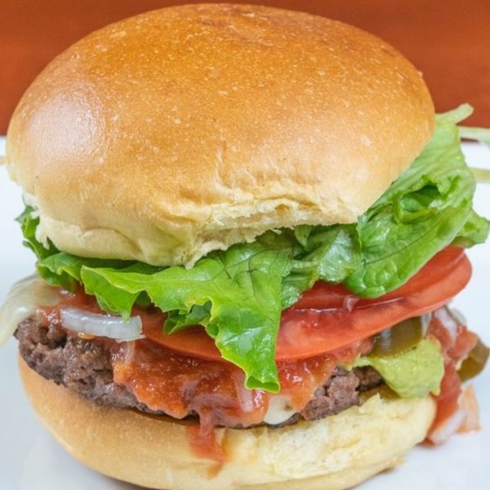 A Texas Ranger burger with lettuce, tomato, onions, guacamole, and jalapeños on a bun.