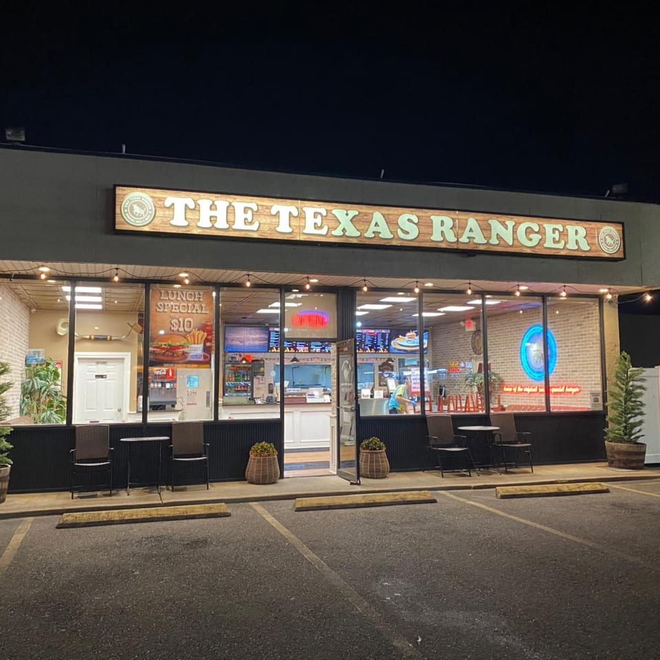 Exterior of The Texas Ranger burger restaurant at night, with illuminated sign and interior visible through windows.